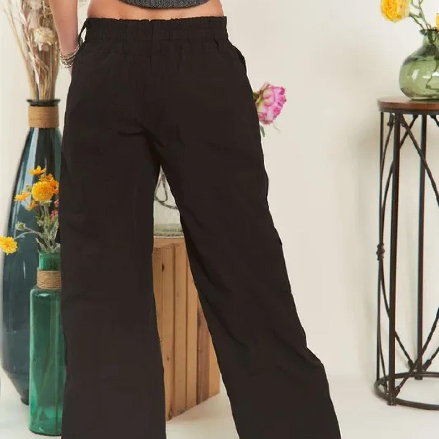 Person wearing black wide-leg pants in a room with decorative vases and flowers.