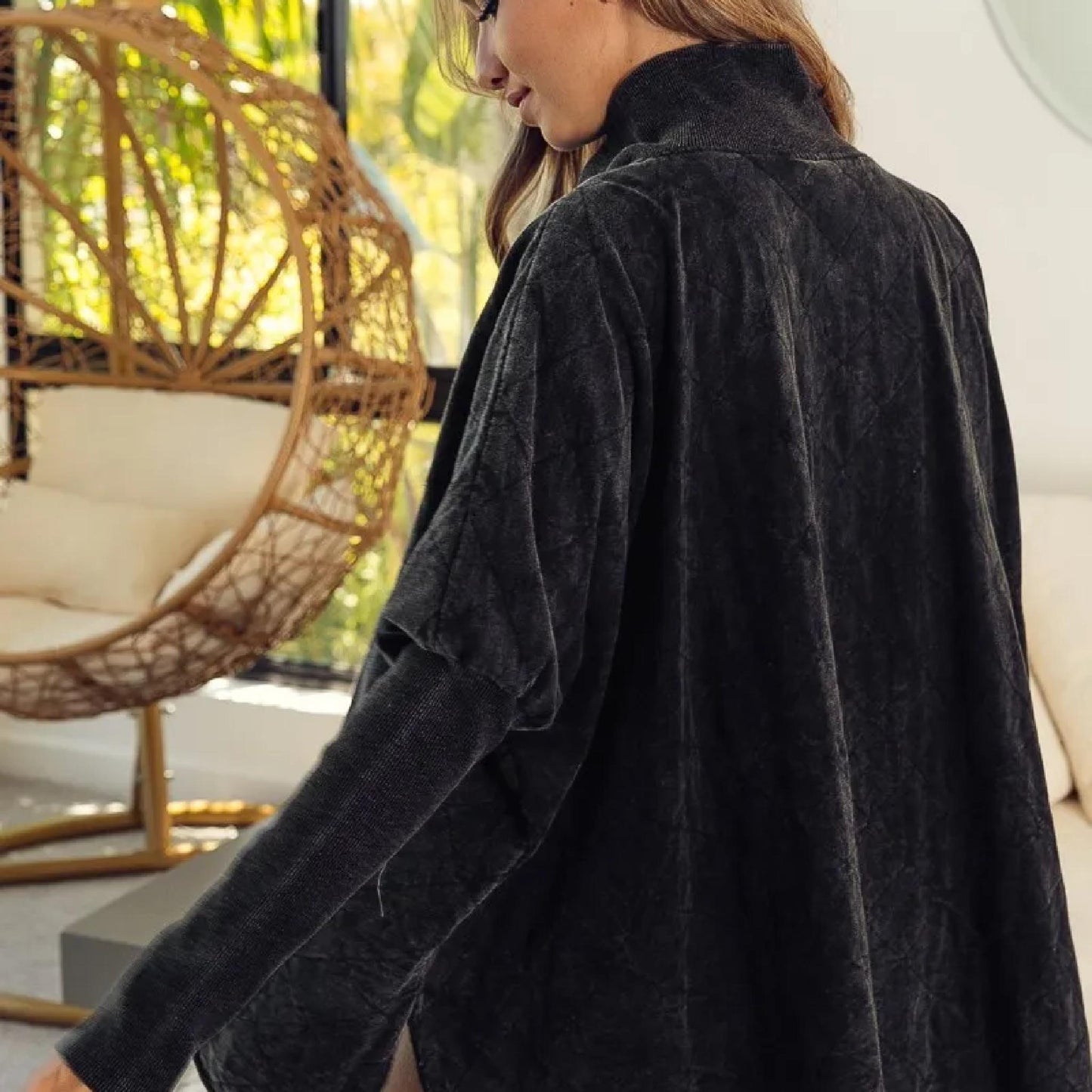 Person wearing a dark gray textured shirt in an outdoor setting with a wicker chair and greenery.