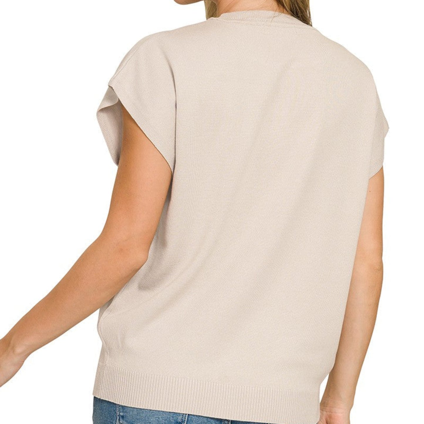 Woman wearing a beige short-sleeve top and blue jeans on a white background