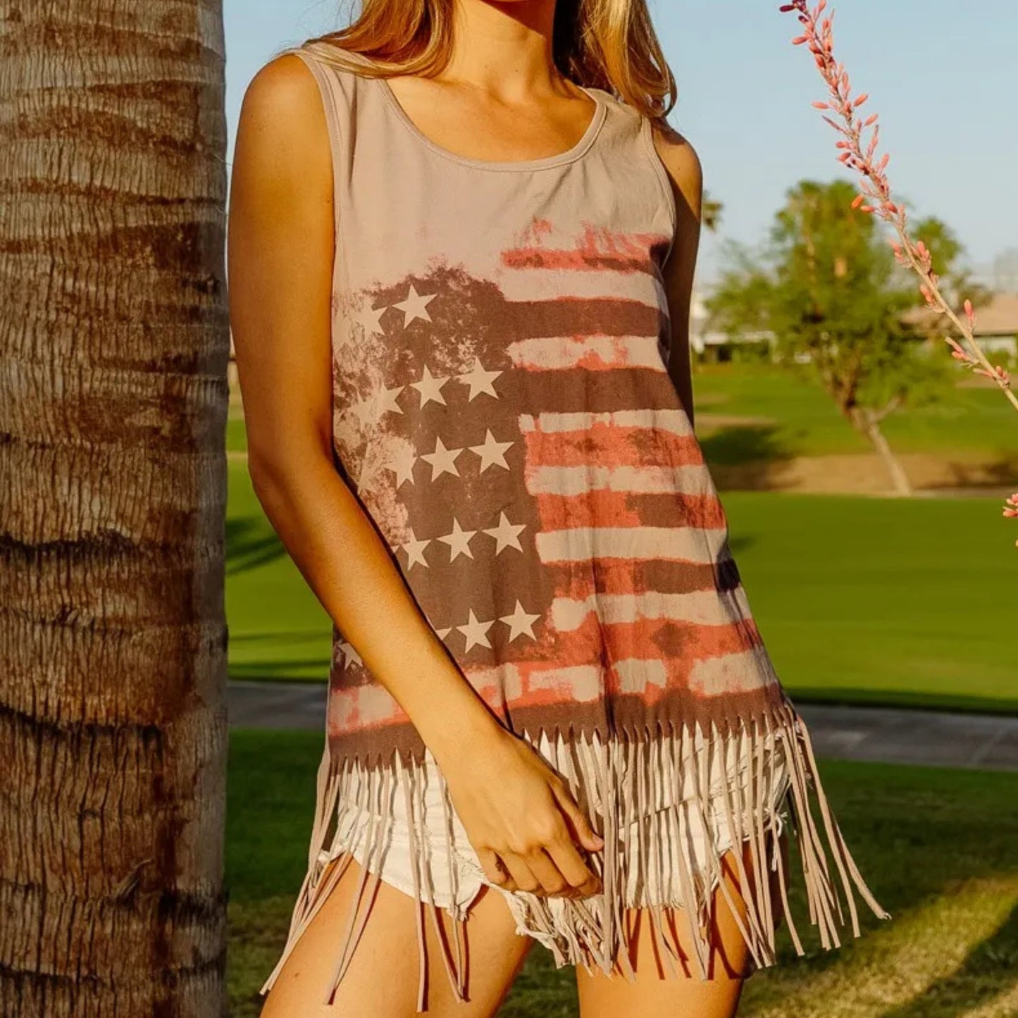 Woman wearing a tank top with an American flag design and fringe details outdoors.