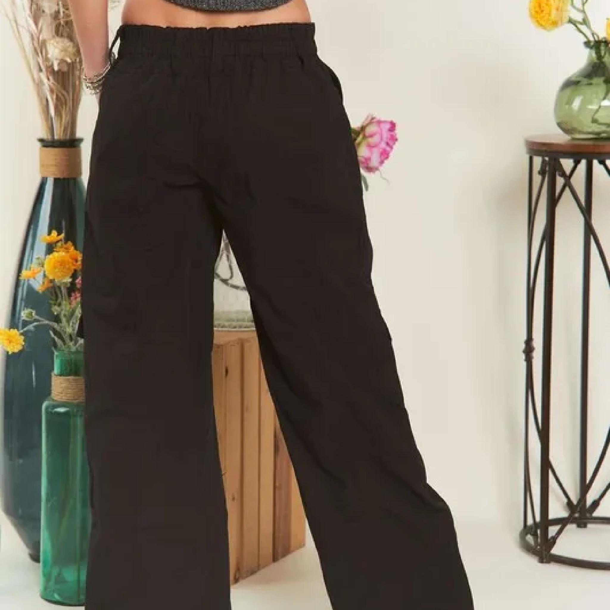 Person wearing black wide-leg pants in a room with decorative vases and flowers.