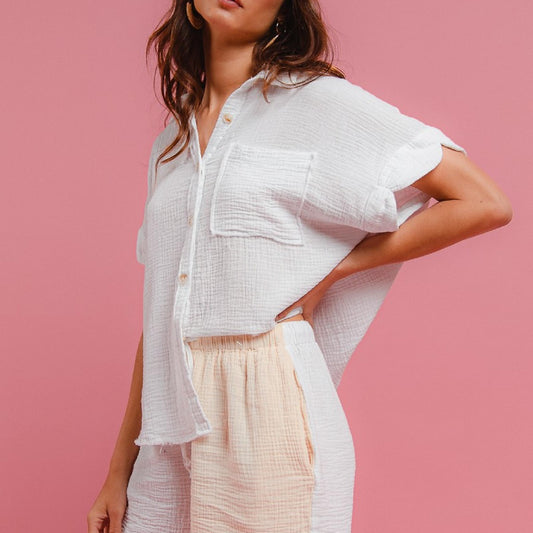 Woman wearing a white shirt and beige shorts with a blue cap on a pink background