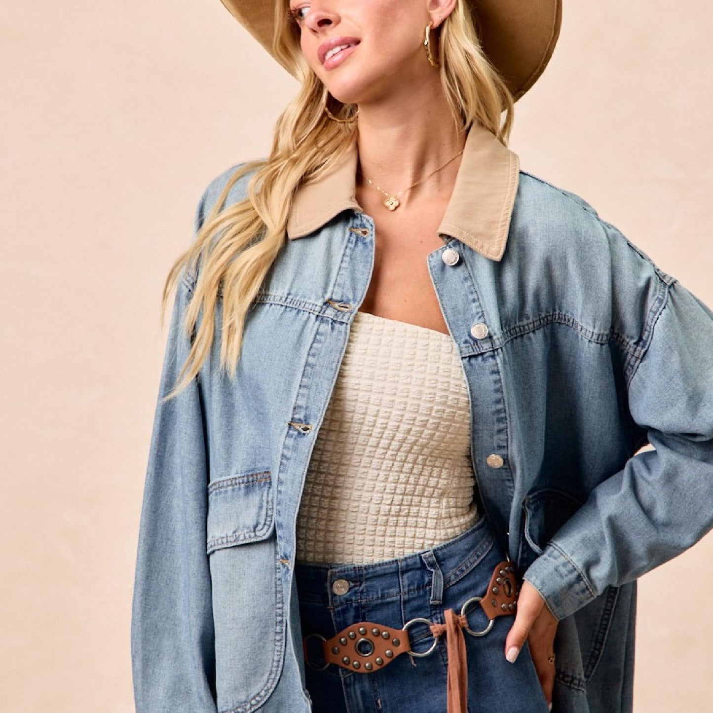 Woman wearing a denim jacket, beige hat, and jeans on a beige background