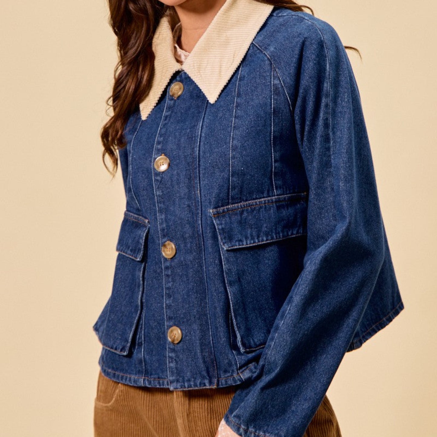 Woman wearing a blue denim jacket with a cream collar and beige hat on a beige background