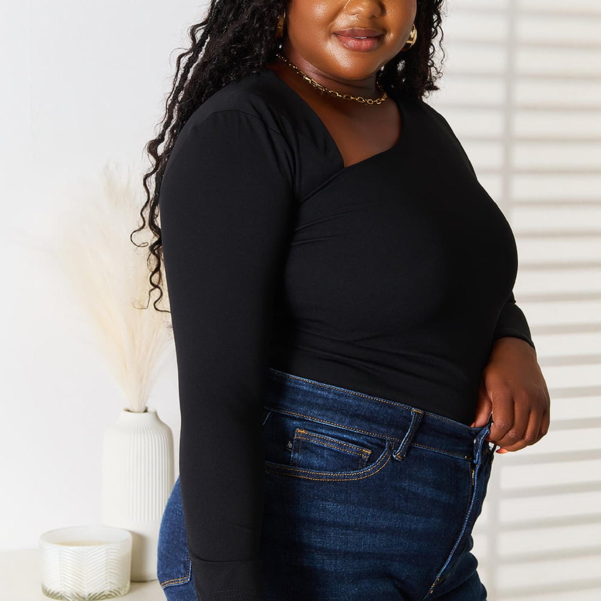 Woman wearing a black top and blue jeans standing indoors with a neutral background