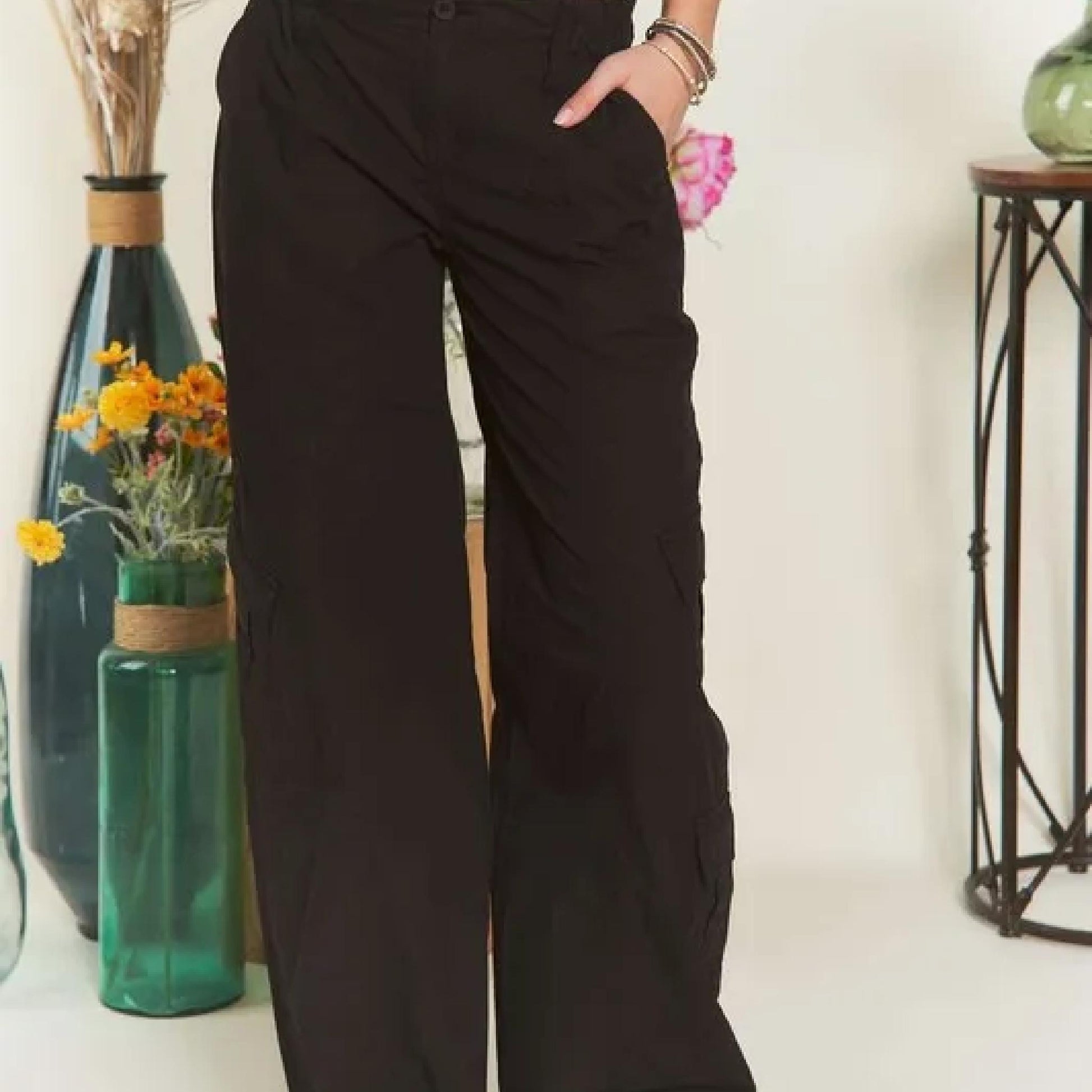 Person wearing black wide-leg pants standing in a room with decorative vases and flowers.