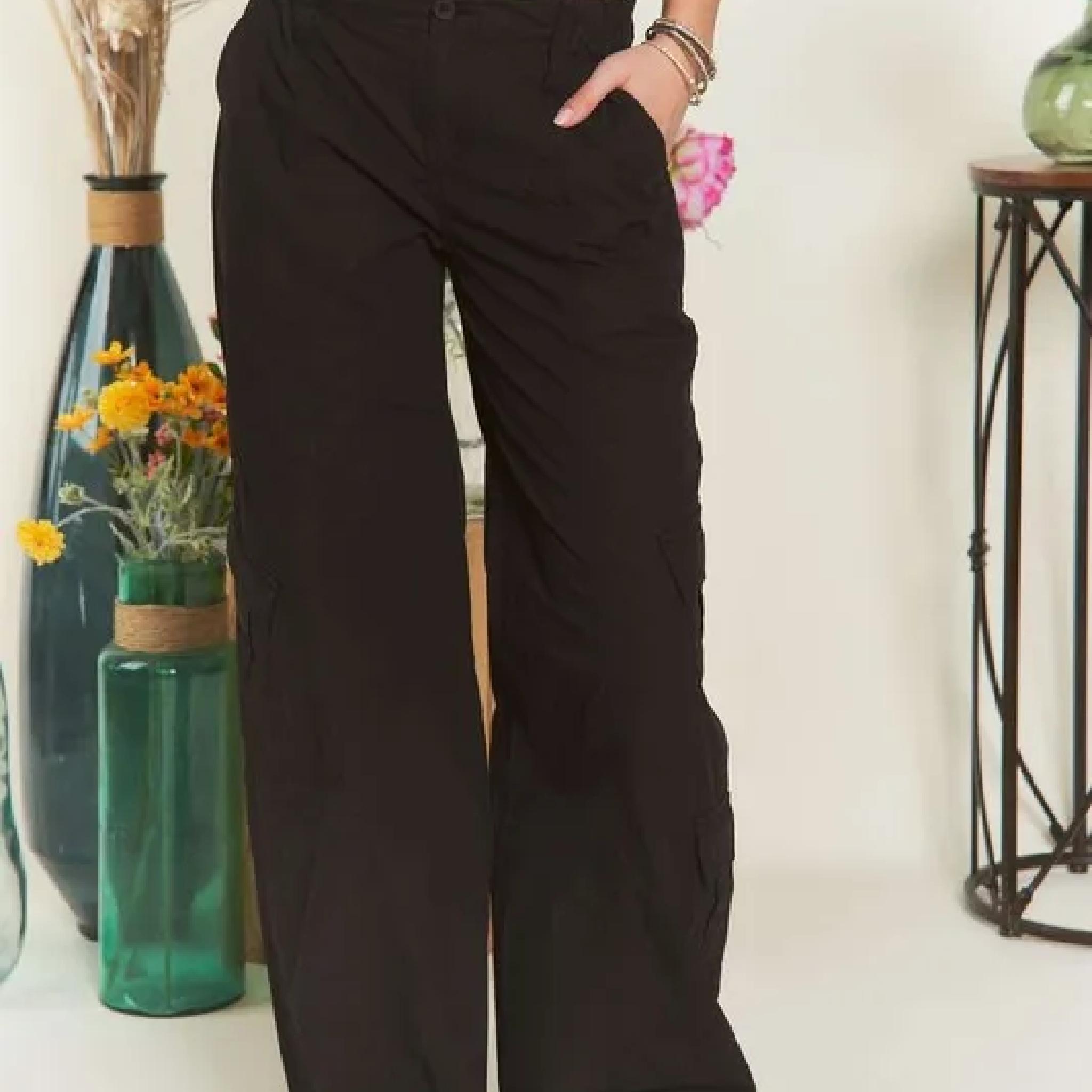 Person wearing black wide-leg pants standing in a room with decorative vases and flowers.