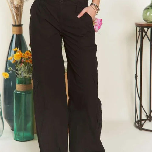 Person wearing black wide-leg pants standing in a room with decorative vases and flowers.