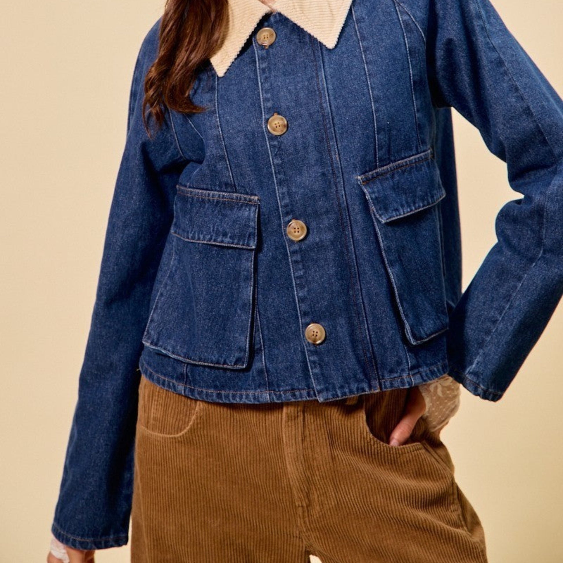Woman wearing a blue denim jacket with a beige collar and brown pants on a beige background