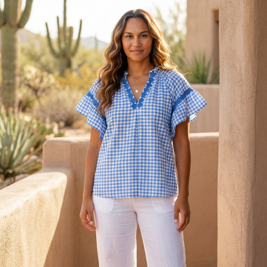 Woman wearing a Umgee blue checkered top and white pants standing in a desert setting with cacti.