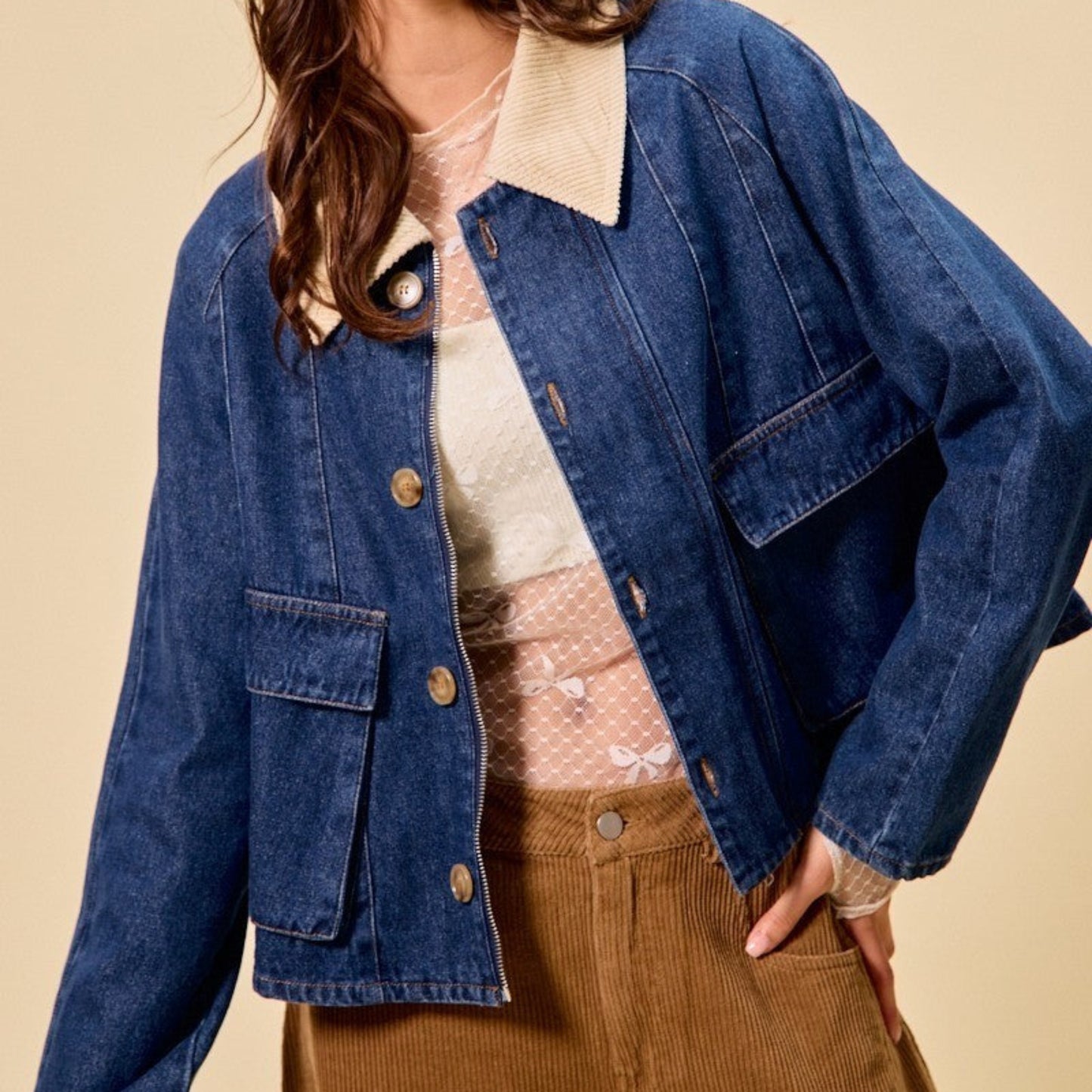 Woman wearing a blue denim jacket over a beige sweater and brown pants on a beige background