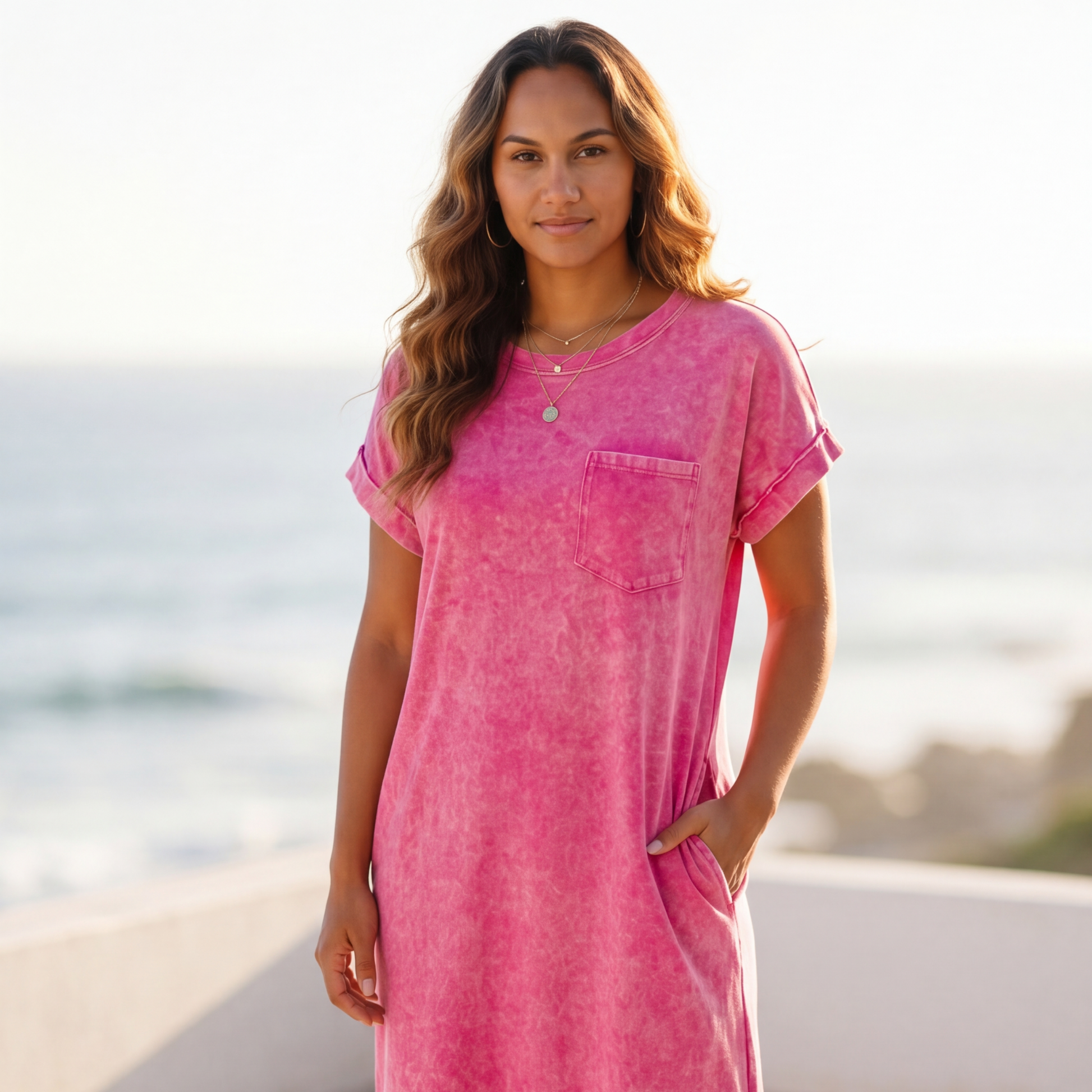 Woman wearing a pink dress standing on a beach with ocean in the background