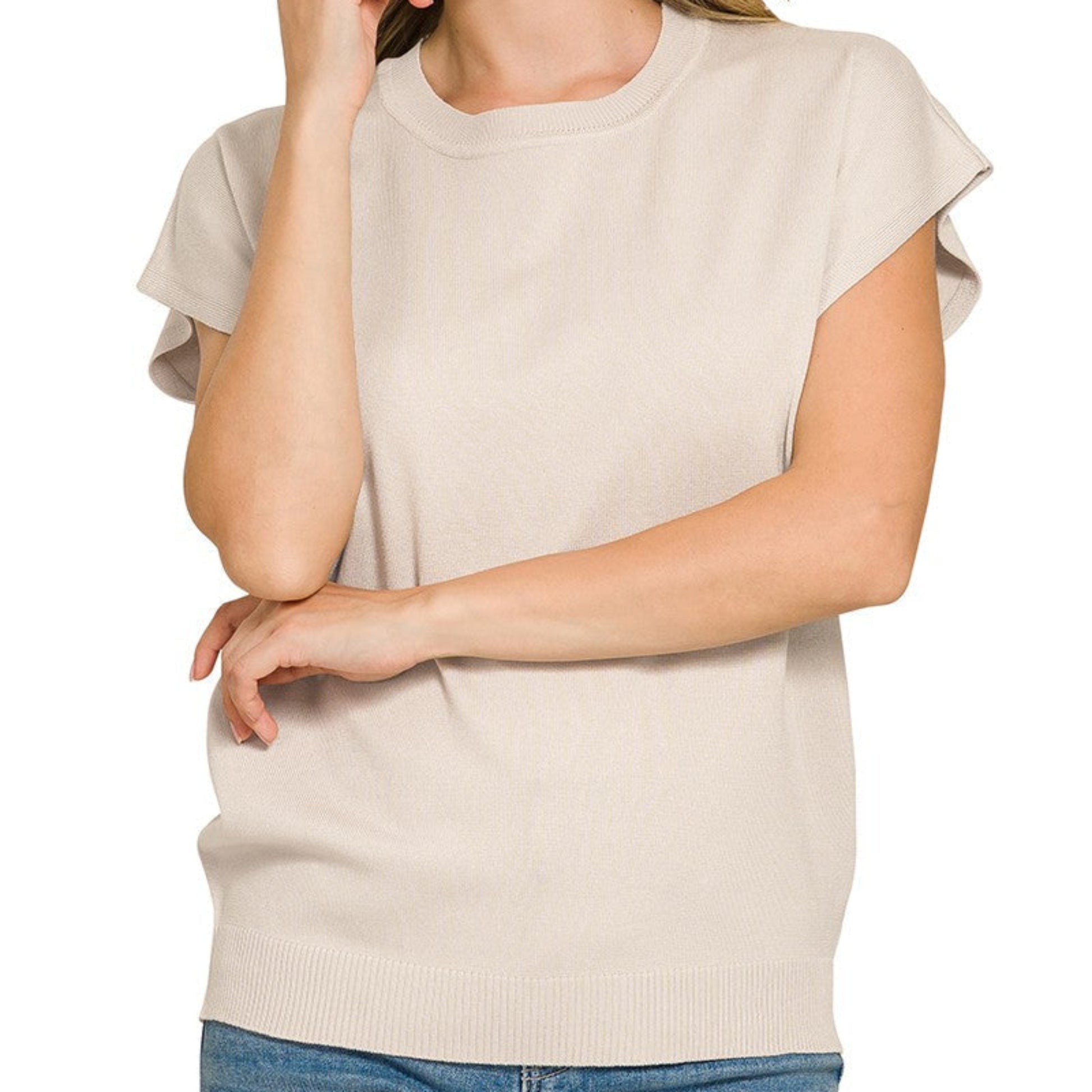 Woman wearing a beige sleeveless top and blue jeans on a white background
