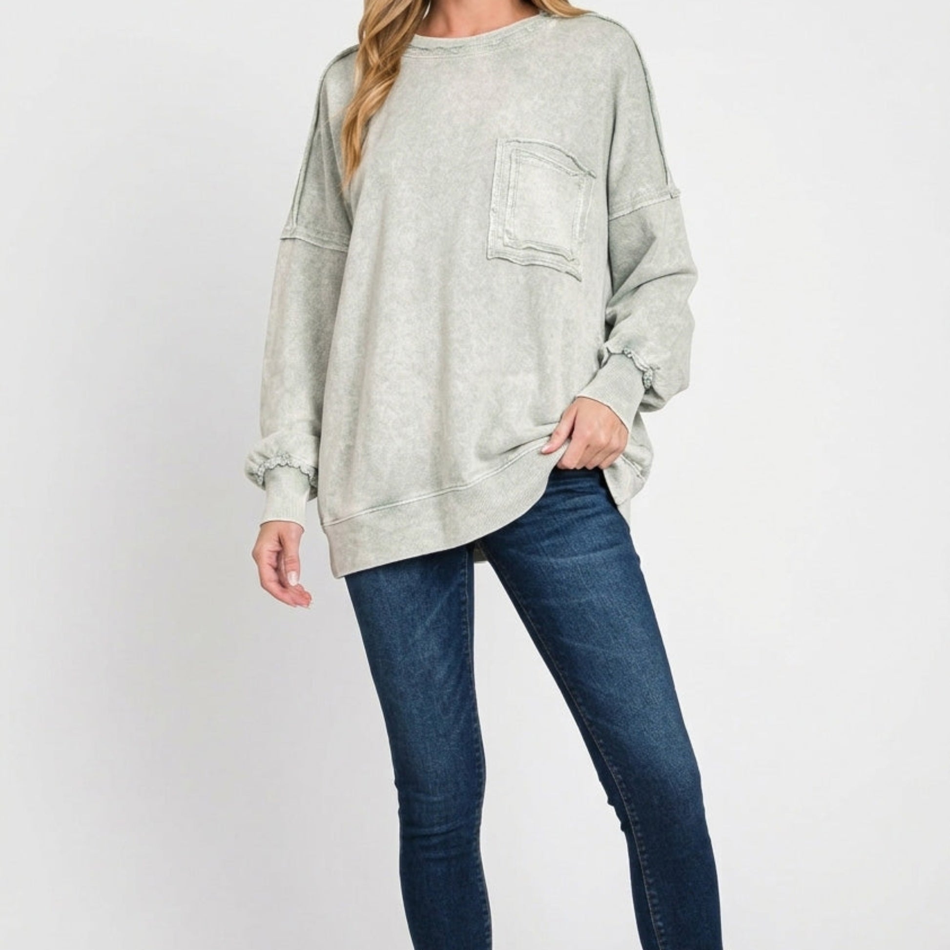 Woman wearing a light gray oversized sweater and blue jeans on a white background