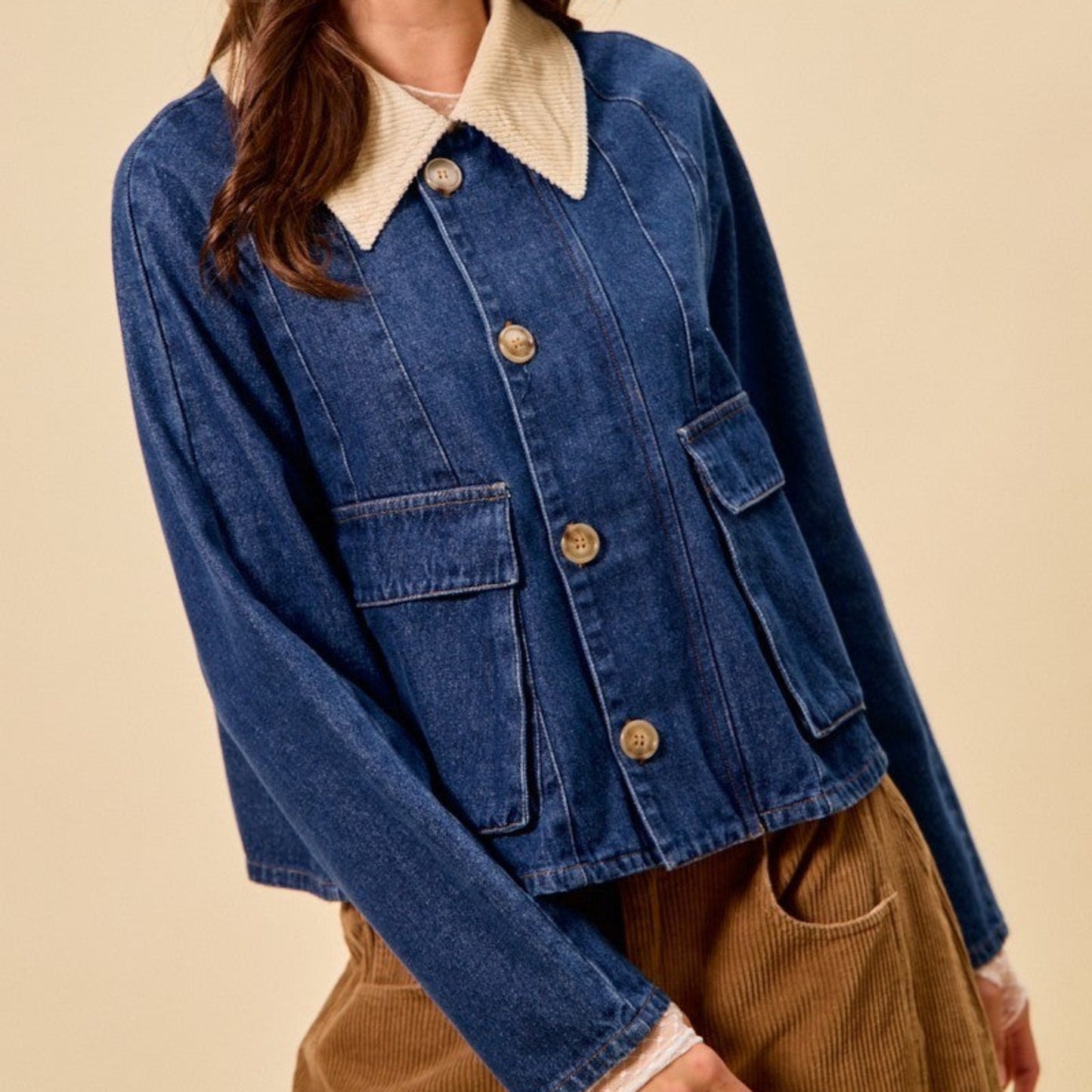 Woman wearing a blue denim jacket with a cream collar and beige pants against a beige background