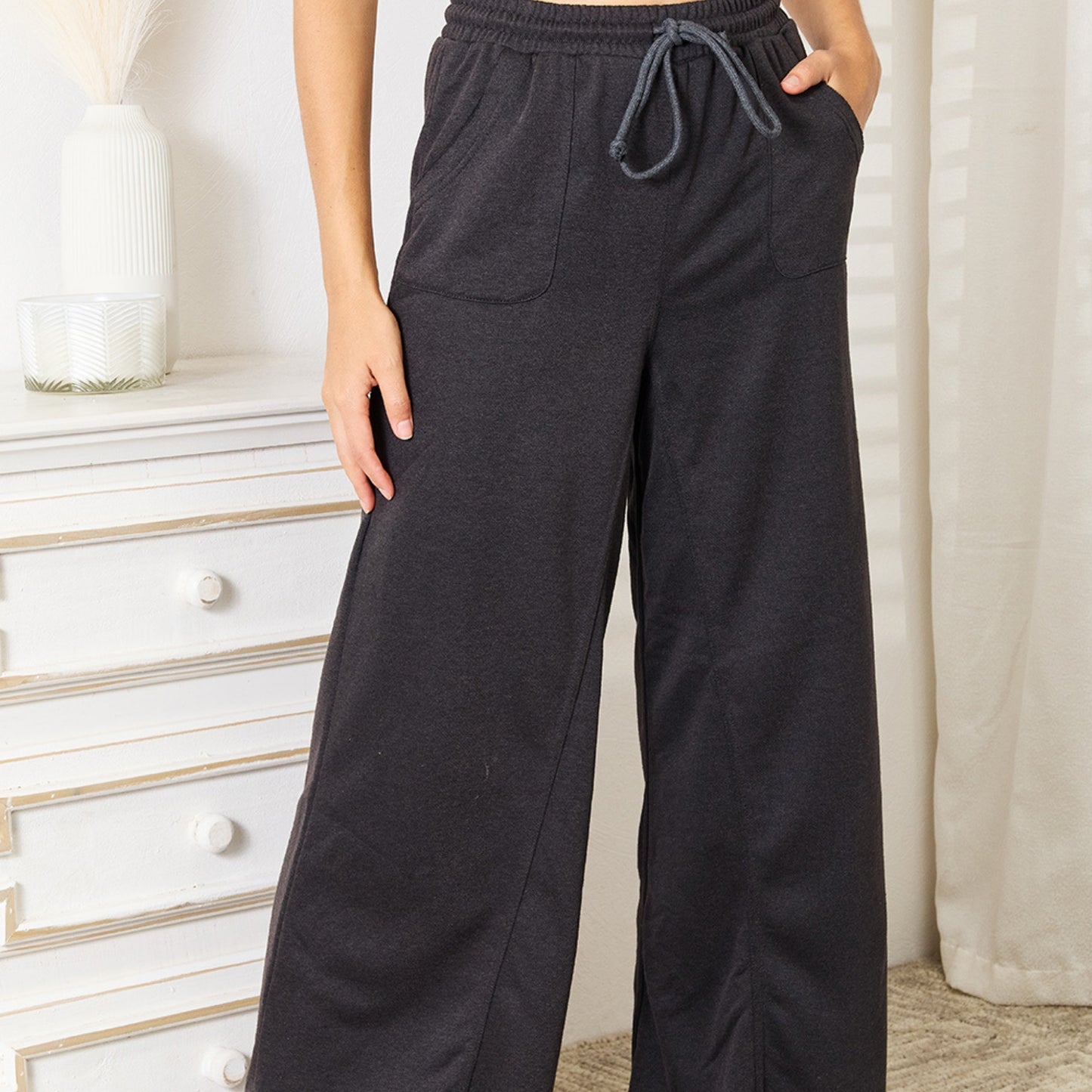 Person wearing dark gray sweatpants in a room with white furniture and curtains.