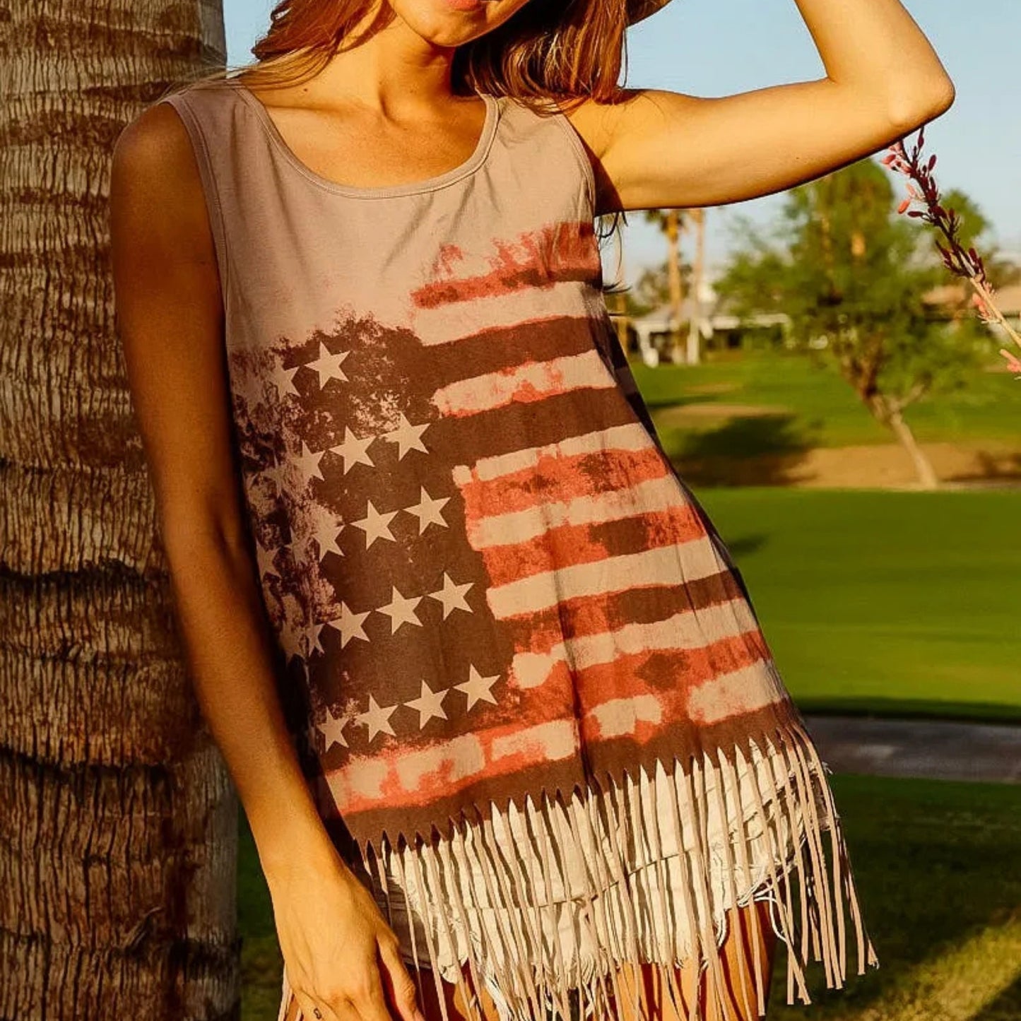Person wearing a tank top with an American flag design and fringes, standing outdoors.
