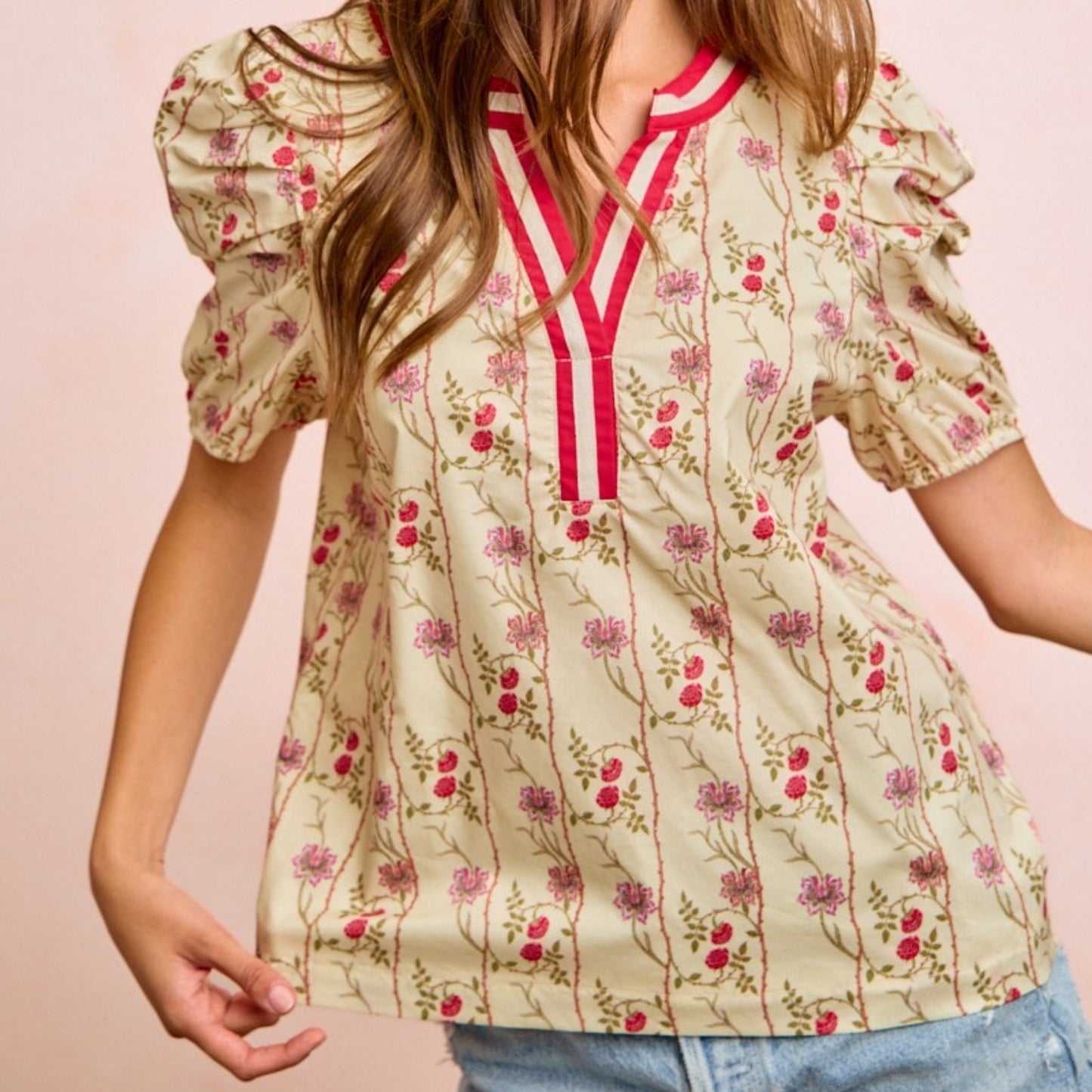 Woman wearing a floral blouse with a pink and white striped collar against a pink background