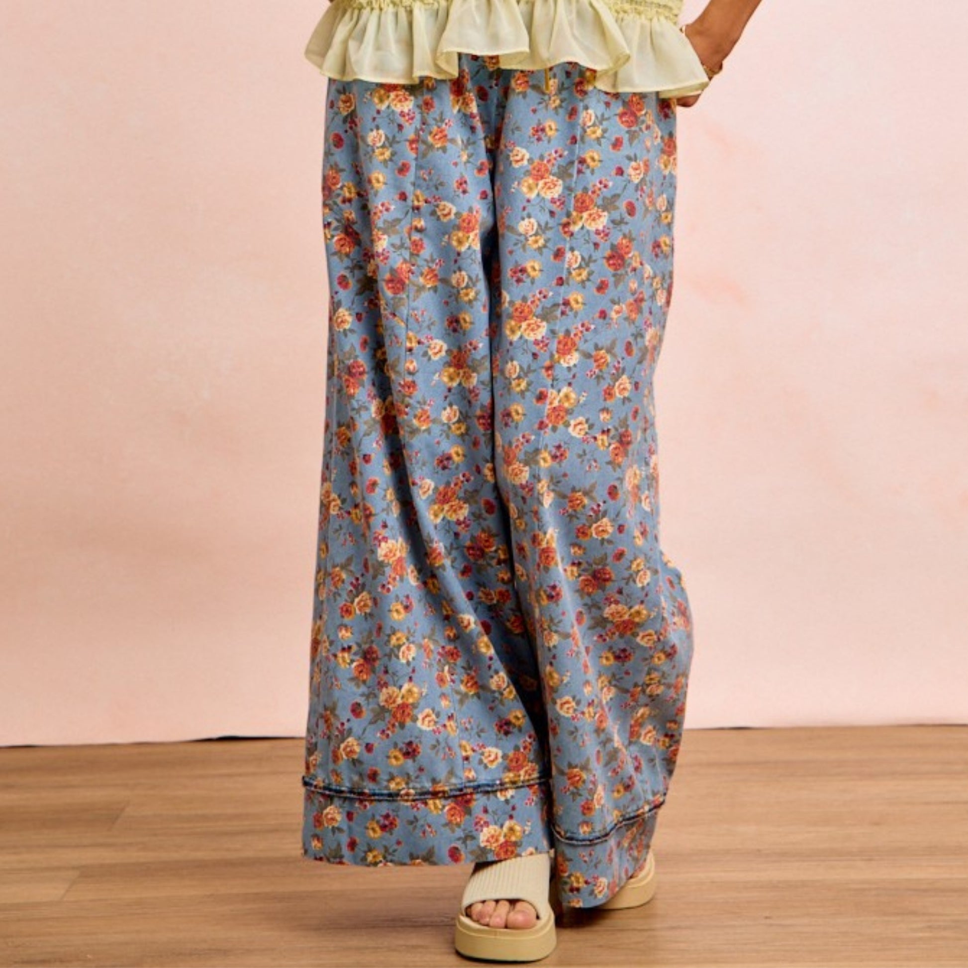 Floral patterned pants worn by a person on a wooden floor with a pink background
