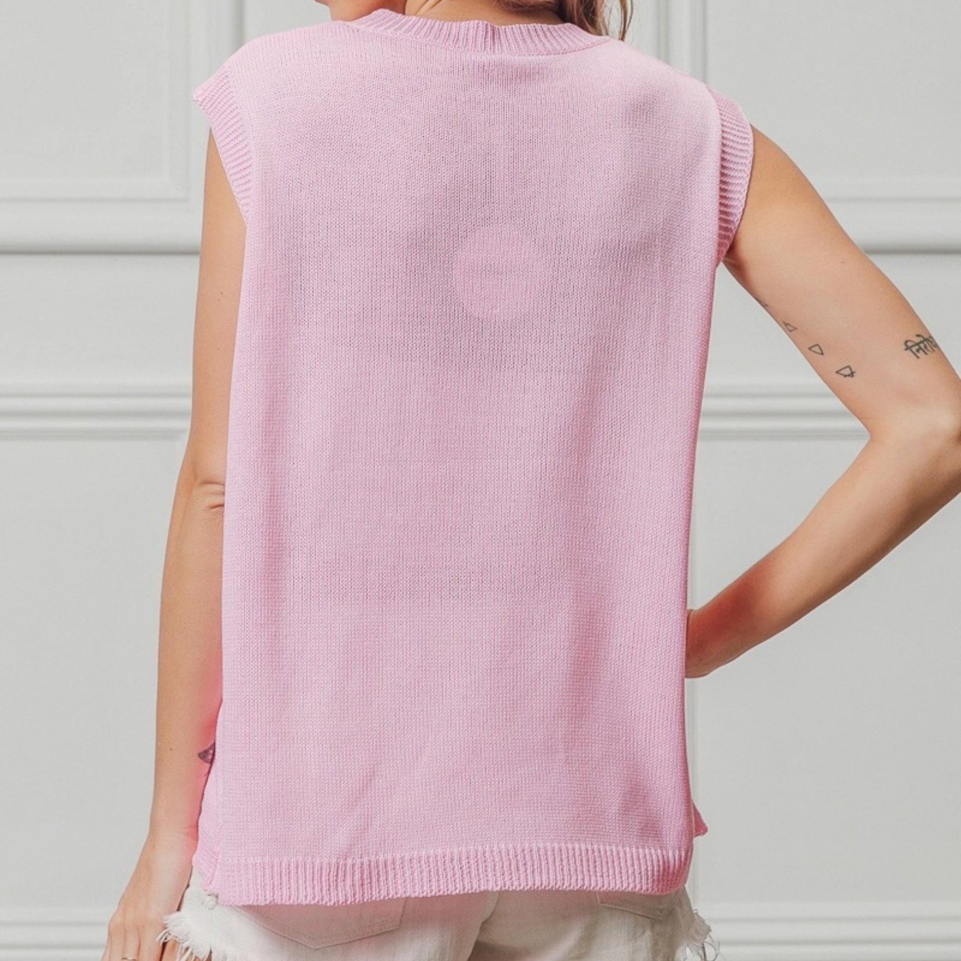 Person wearing a pink sleeveless sweater against a white background