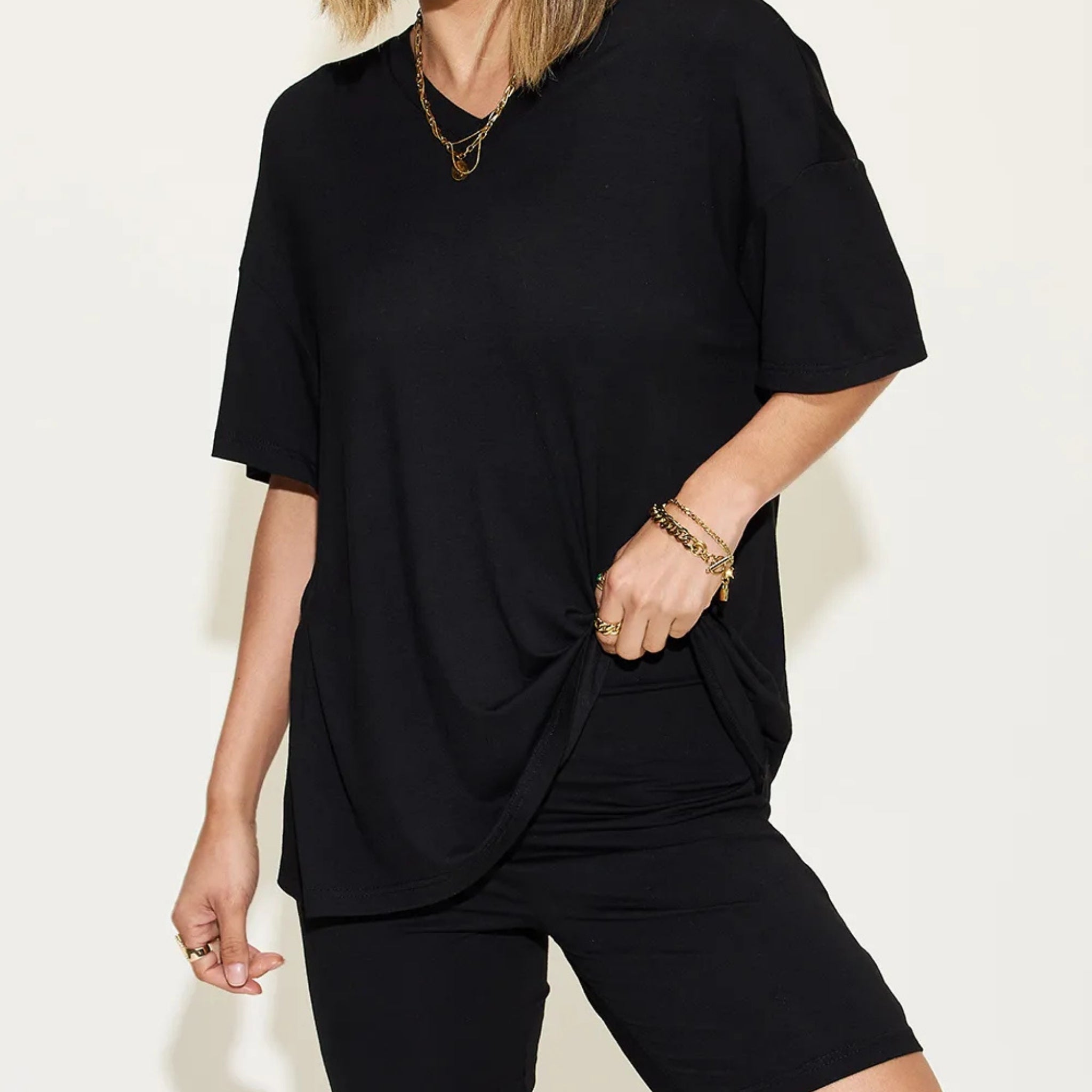 Person wearing a black outfit with gold jewelry against a white background