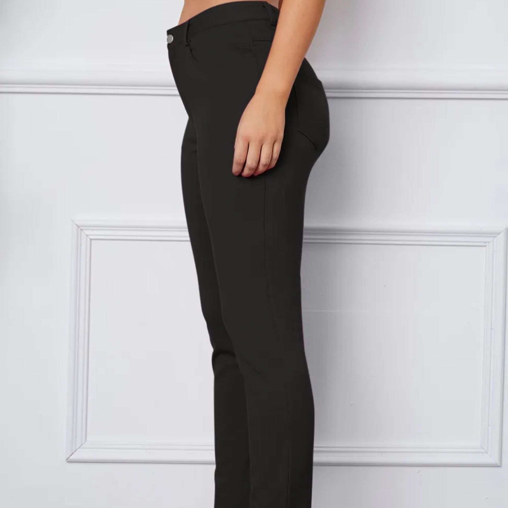 Black pants worn by a person against a white paneled wall
