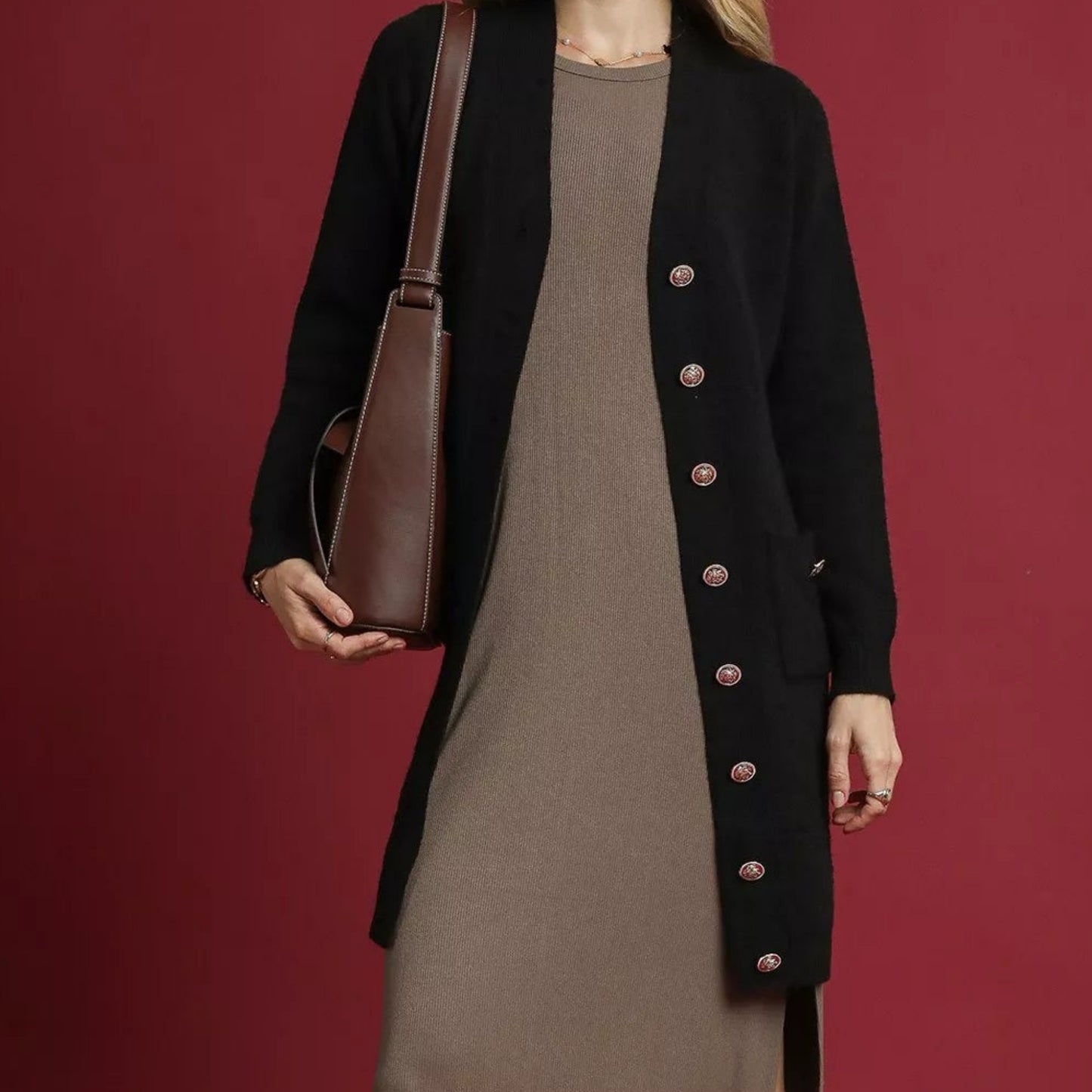 Person wearing a black coat with red buttons holding a brown leather bag against a red background