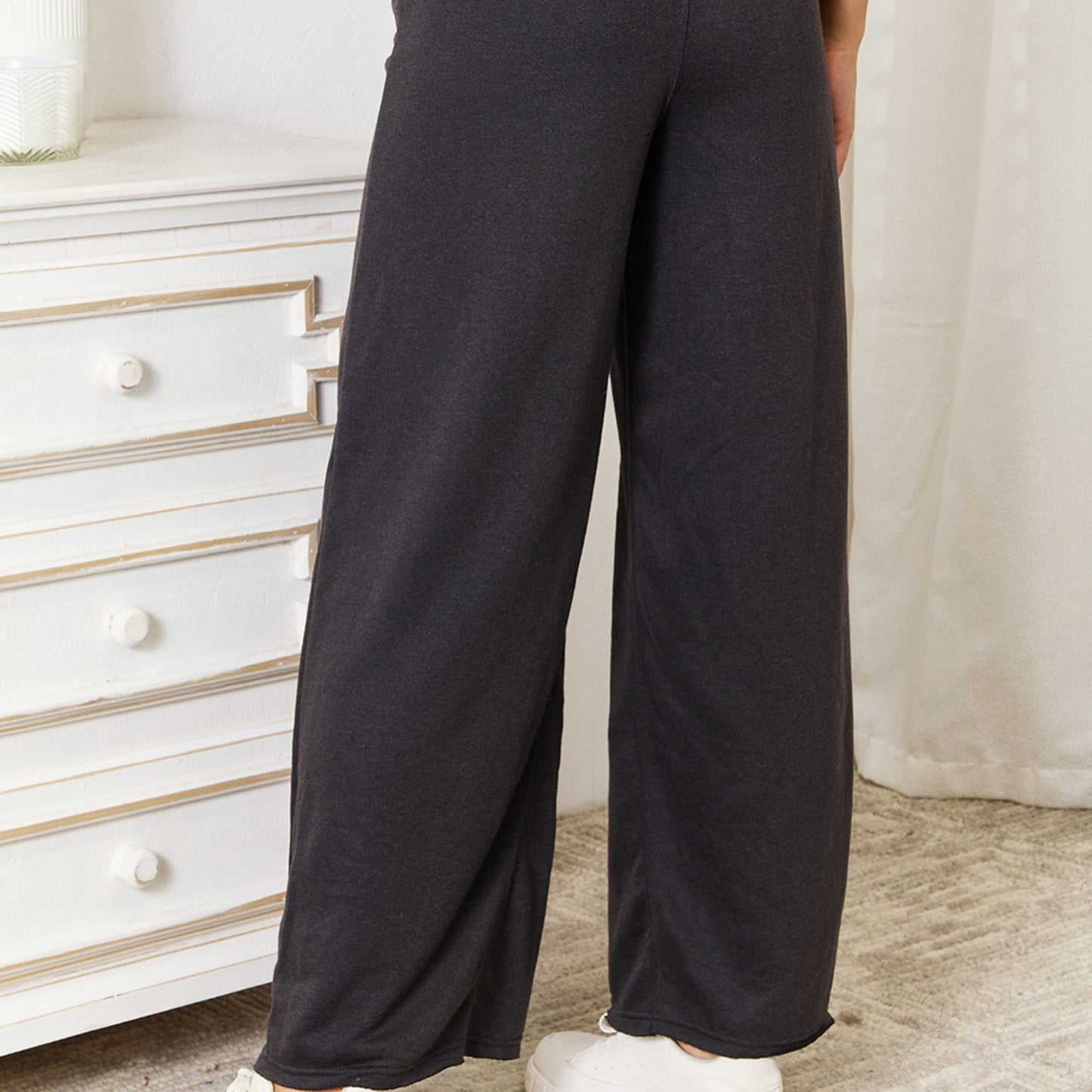 Person wearing dark gray wide-leg pants standing in front of a white dresser.