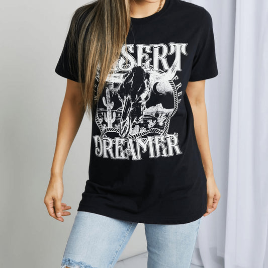 Frontal display of a woman wearing a black 'Desert Dreamer' tee with a beige hat.