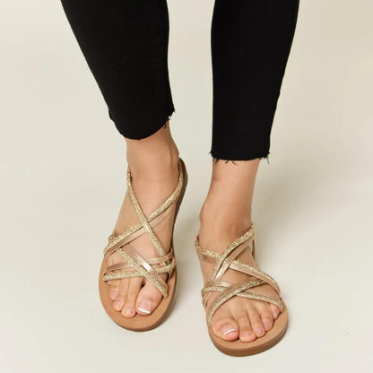 Front view of Forever Link gold rhinestone crisscross flat sandals worn with black trousers.