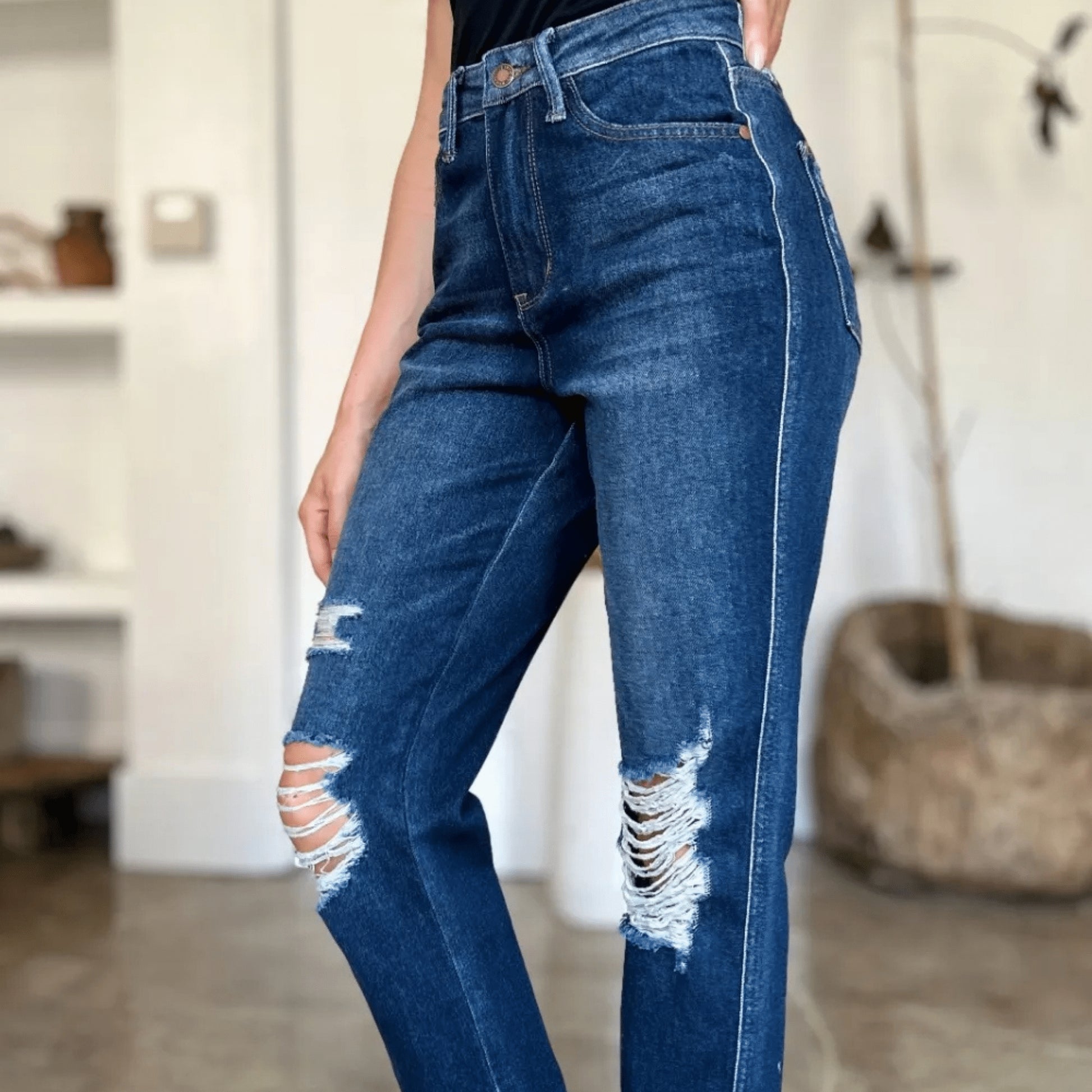 Side view of heavy destroy straight-leg jeans and white sneakers.