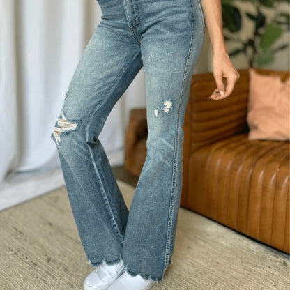 Full body shot of a person wearing Judy Blue flare jeans and a white top.