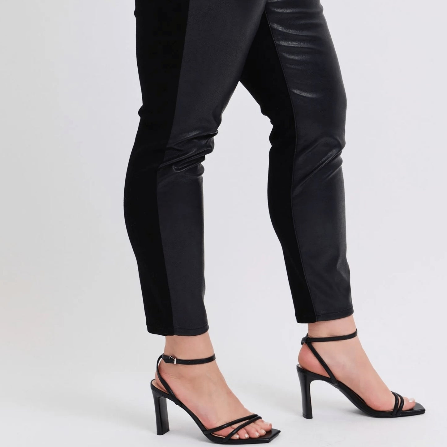 Black high-heeled sandals worn with black pants on a white background