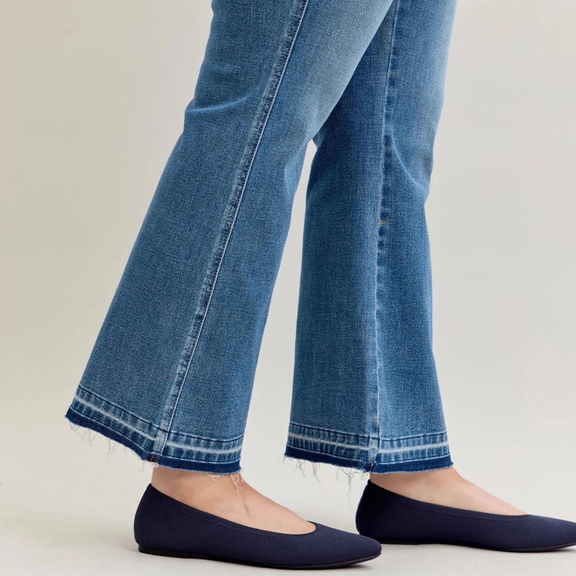 Side view of slim bootcut jeans with release hem detail and navy flats.