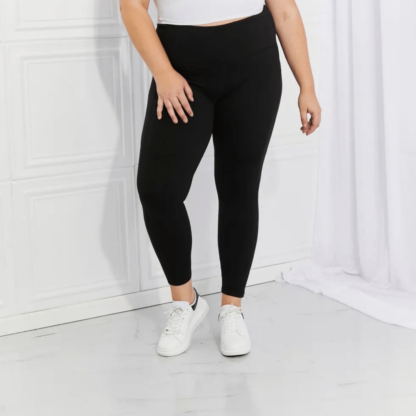 Complete presentation of black performance leggings with white sneakers on a white background.