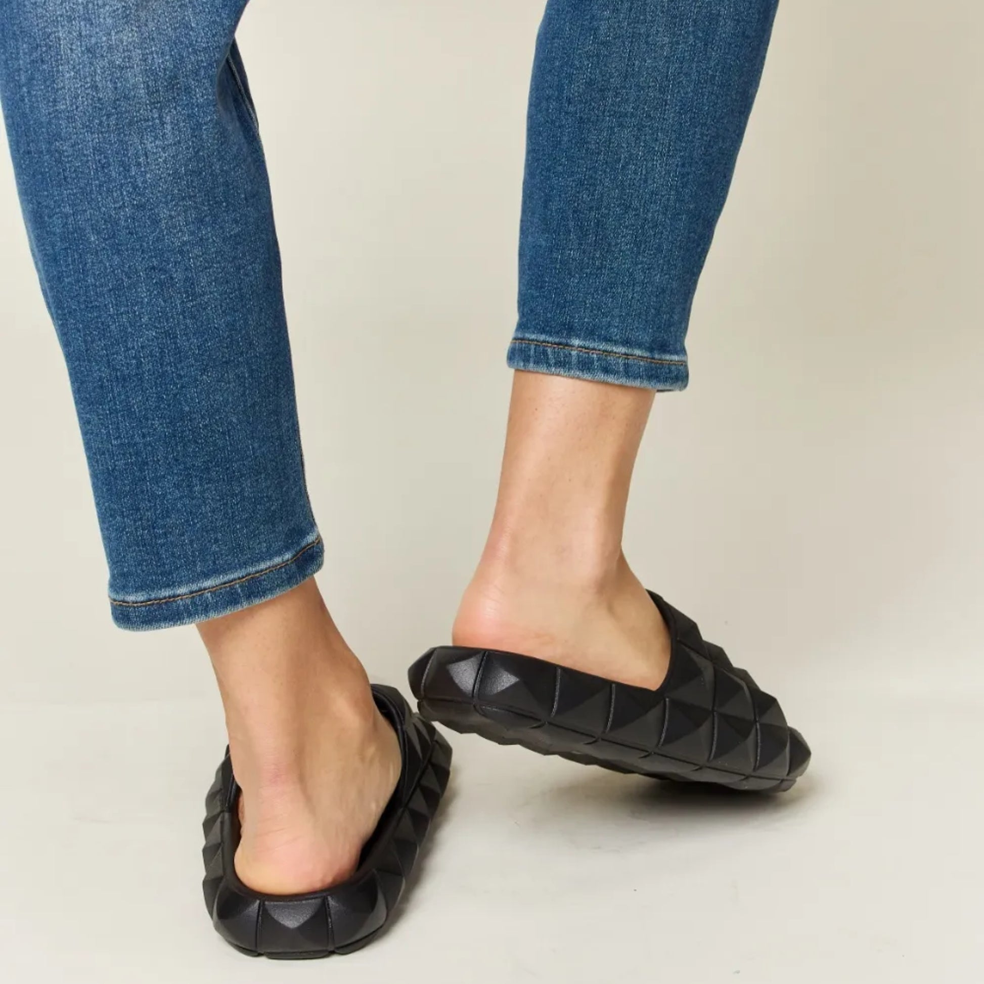 Black quilted sandals worn with blue jeans on a neutral background