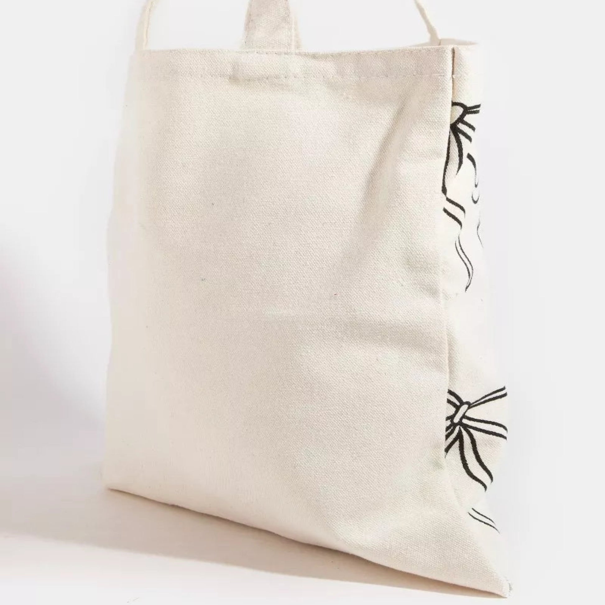 Close-up detail of the ribbon bow tie print tote bag fabric and delicate bow graphic