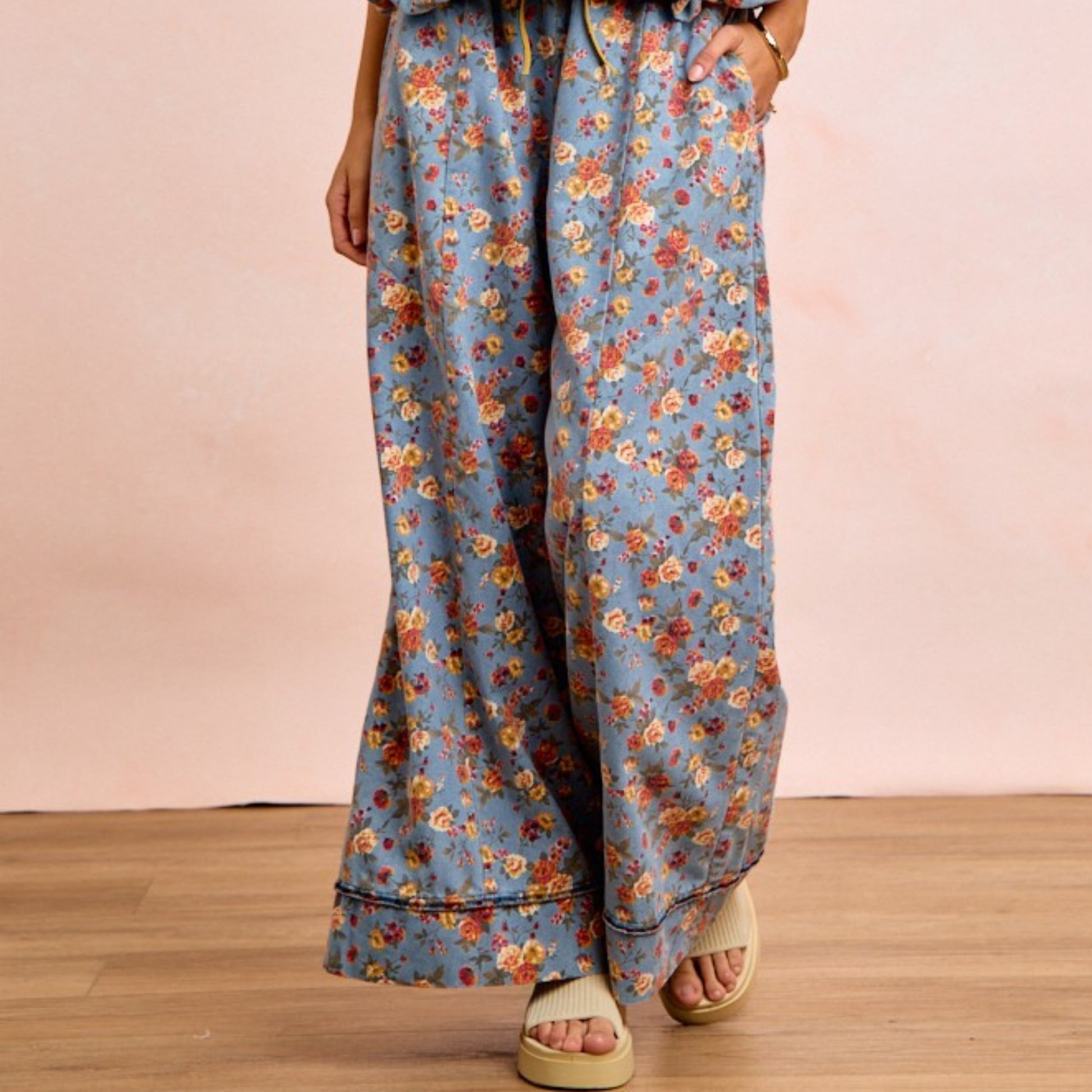 Floral patterned pants worn by a person on a wooden floor with a pink wall background