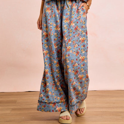 Floral patterned pants worn by a person on a wooden floor with a pink wall background