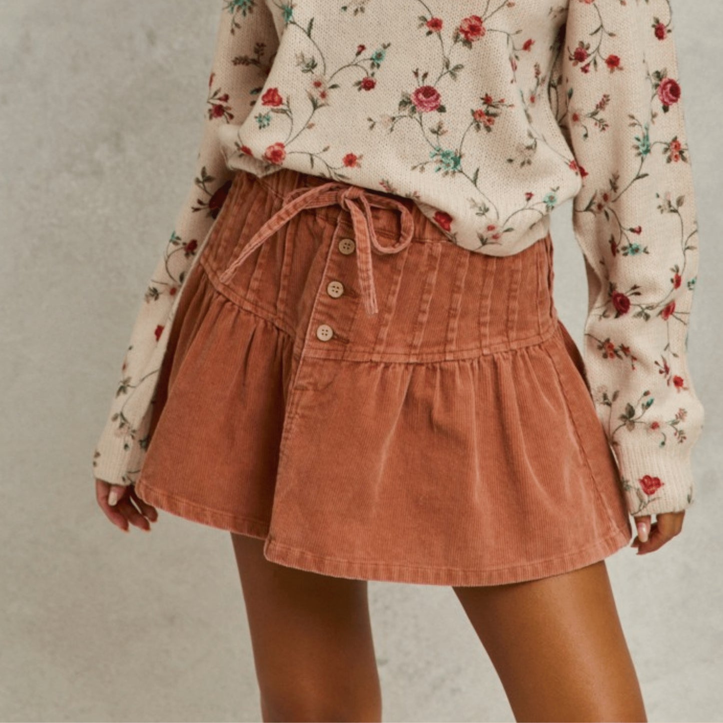 Side view of the SO ME rust corduroy mini skirt with pintuck and flared details.