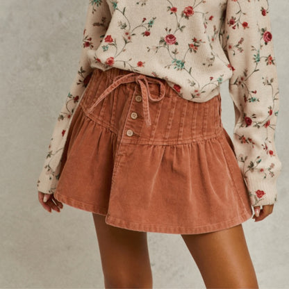 Side view of the SO ME rust corduroy mini skirt with pintuck and flared details.