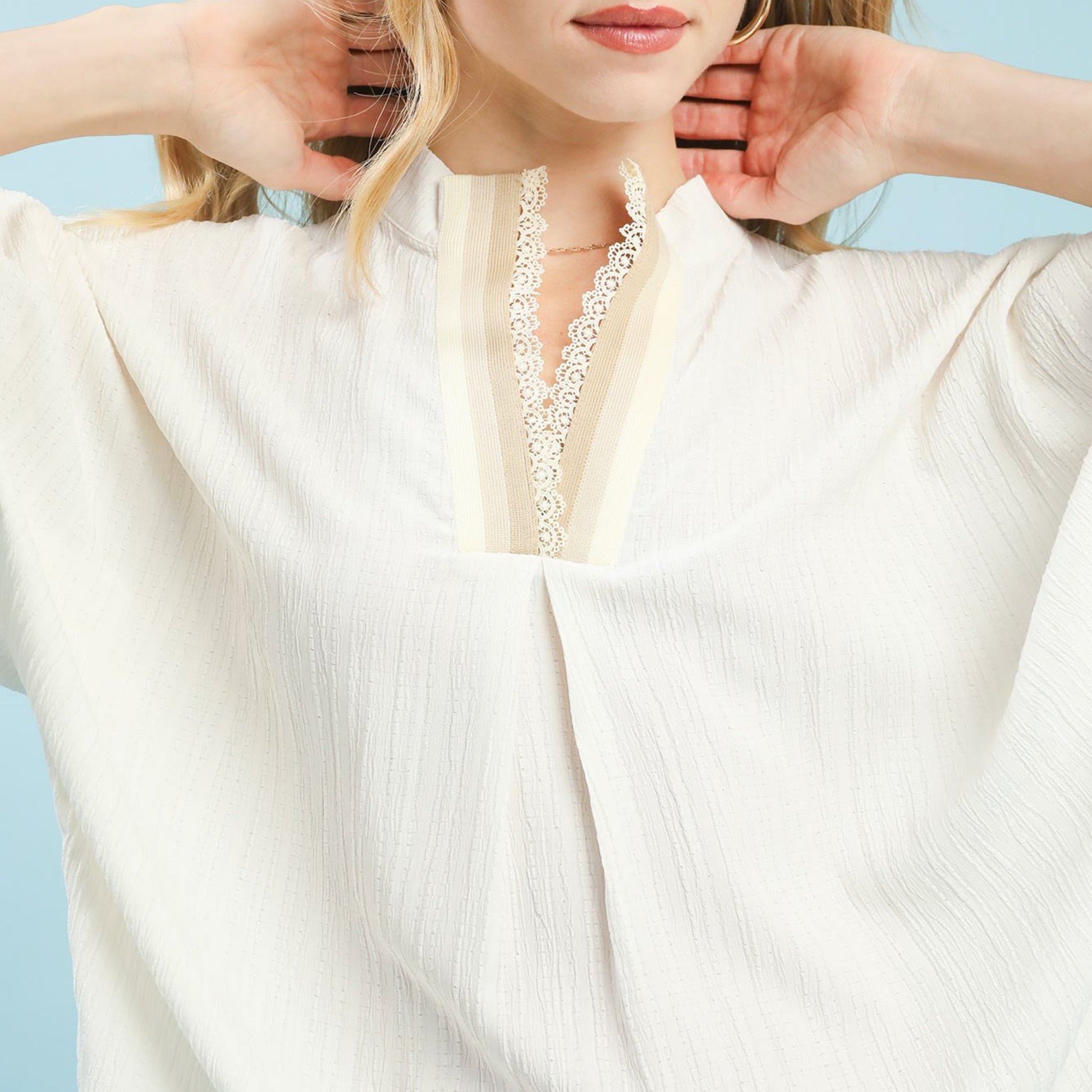 Close-up of the delicate lace trim and textured fabric on the cream blouse.