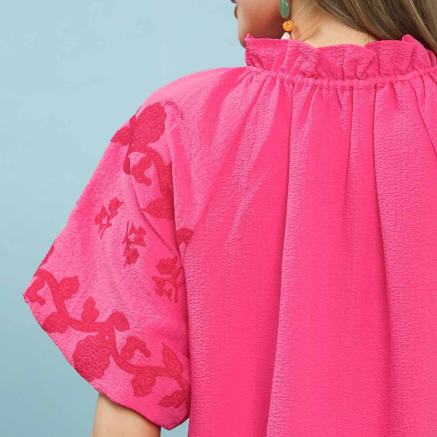 Close-up of a bright pink blouse with floral embroidery on a light blue background