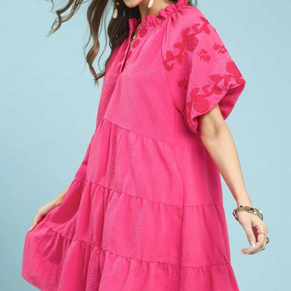 Woman wearing a pink dress with floral patterns against a light blue background