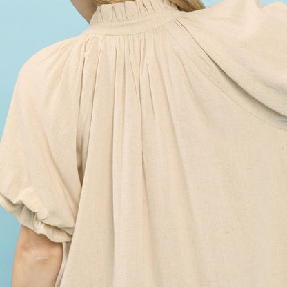 Detail view of the flattering V-neckline and romantic flutter sleeve design on the oatmeal blouse.