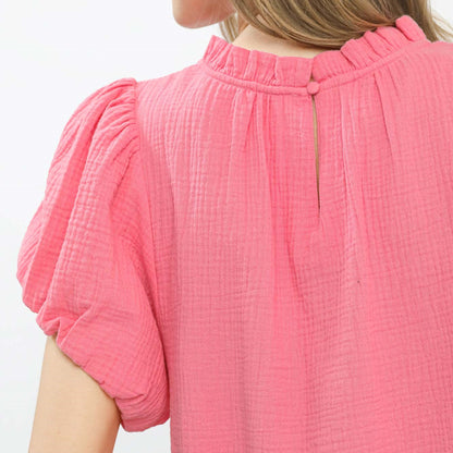 Close-up of the delicate ruffle neck detail and textured gauze fabric in pink.