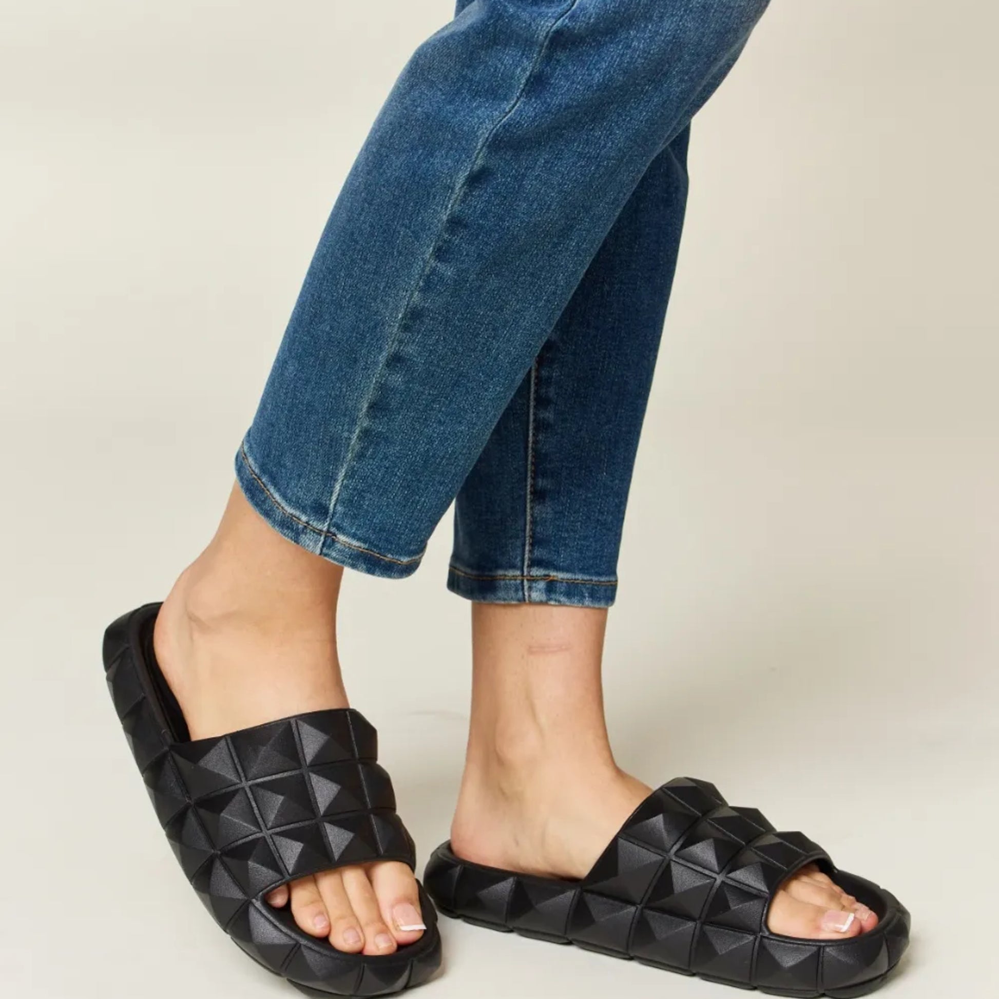 Black quilted sandals worn with blue jeans on a neutral background