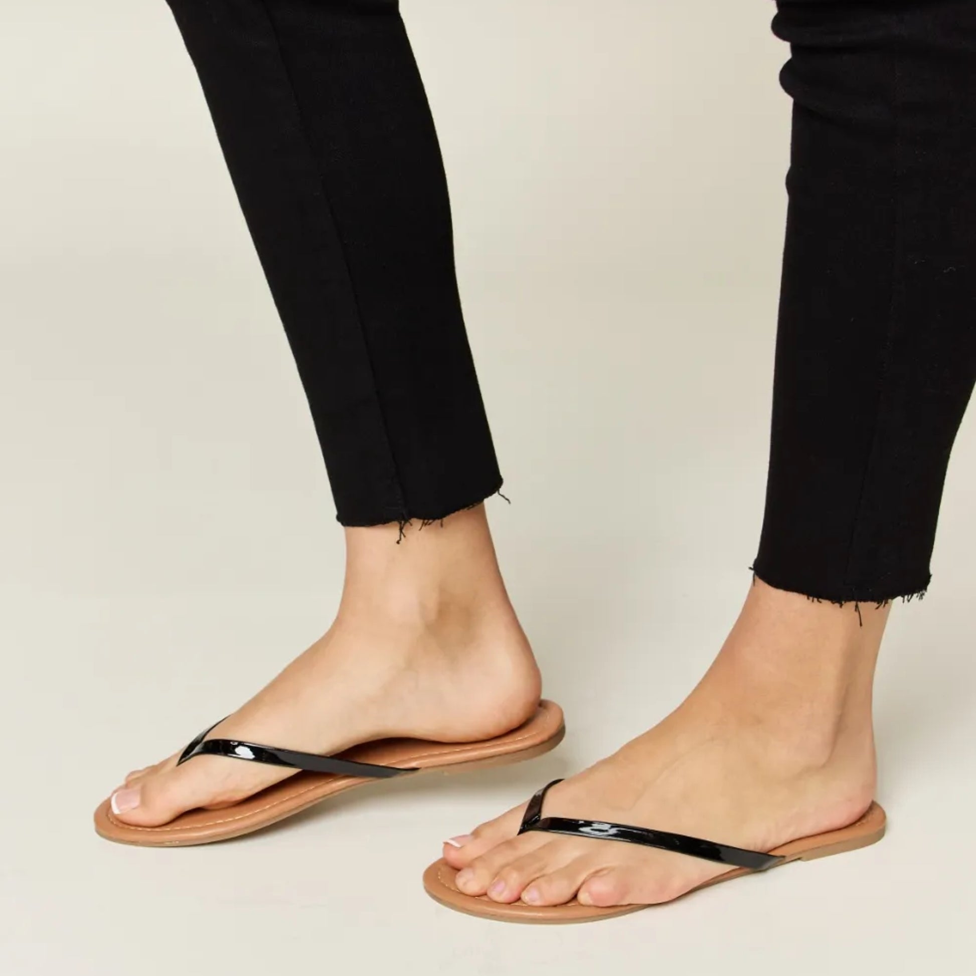Person wearing brown flip-flops with black straps on a neutral background